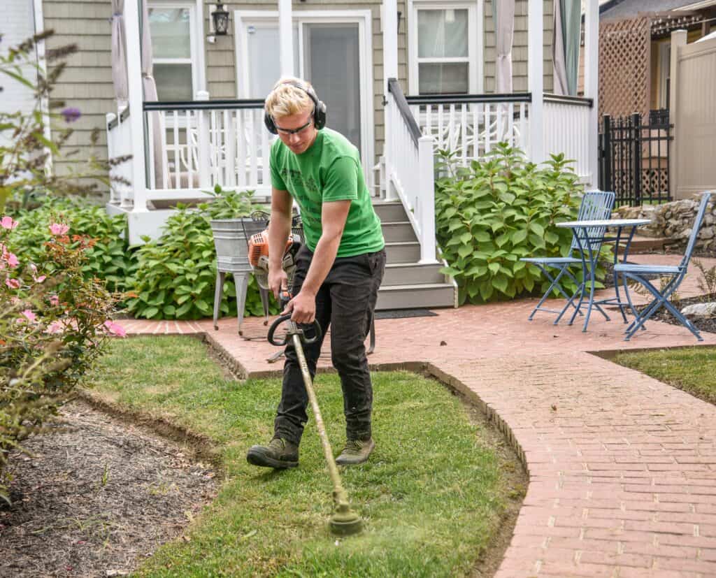 Homme utilisant un outil électrique pour tondre la pelouse dans un jardin.