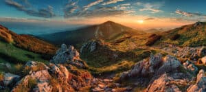 Paysage de montagne au coucher du soleil avec rochers et végétation.